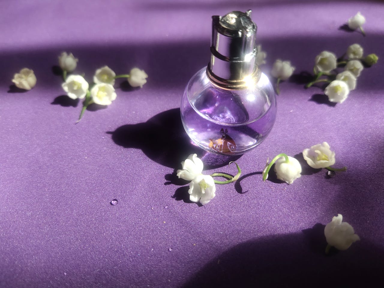 A perfume bottle surrounded by lily of the valley flowers on a purple background, capturing a sense of elegance.