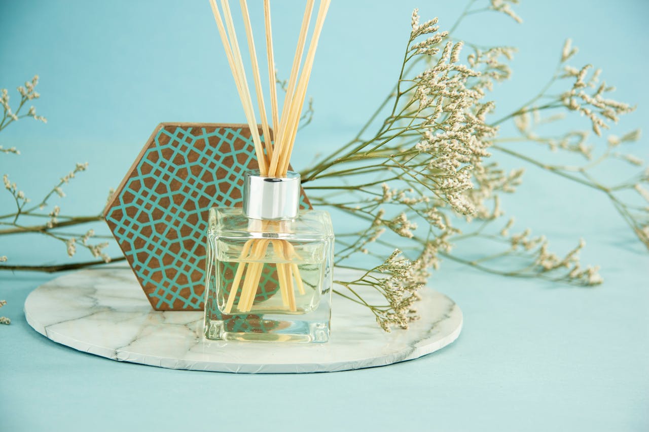 Composition of glass bottle with fluid aroma oil with reed sticks placed near Gypsophila branch and geometric decor on blue background