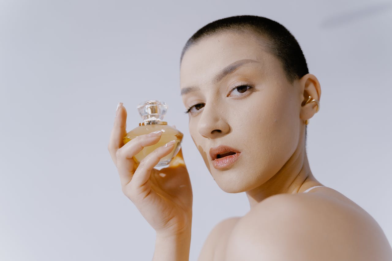 Close-up portrait of a woman with short hair holding a perfume bottle, showcasing elegance and style.